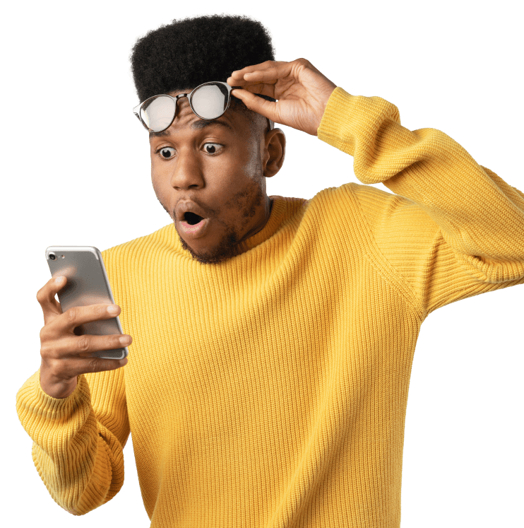 A male lifting up his glasses with a shocked expression looking at the phone in his hand.
